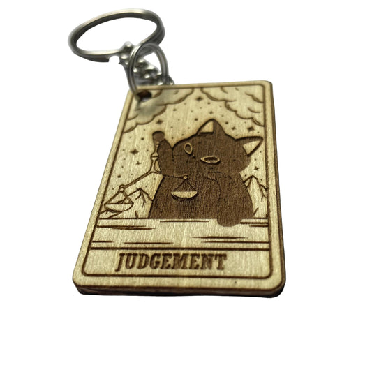 Wooden keychain with a cat illustration and 'Judgement' text on a gray background