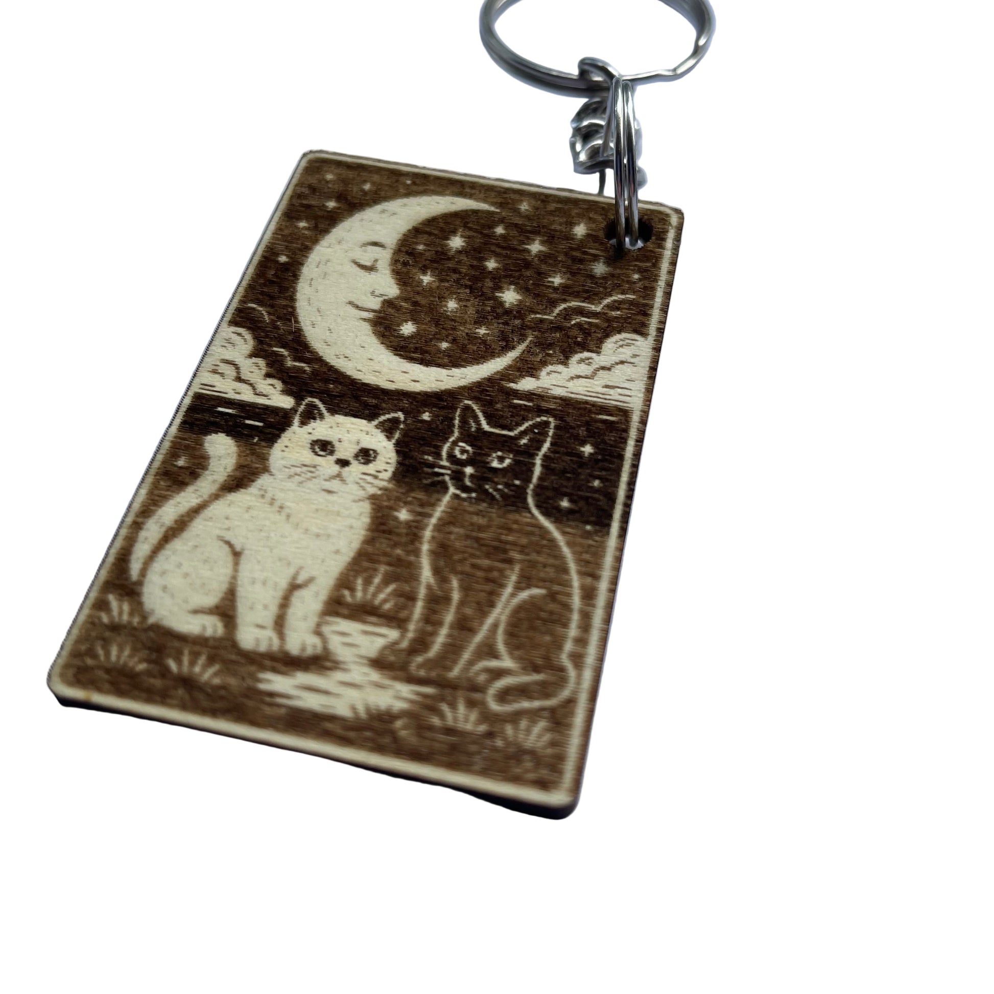 Wooden keychain with engraved design of two cats under a moon and stars on a white background.