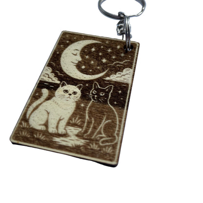 Wooden keychain with engraved design of two cats under a moon and stars on a white background.