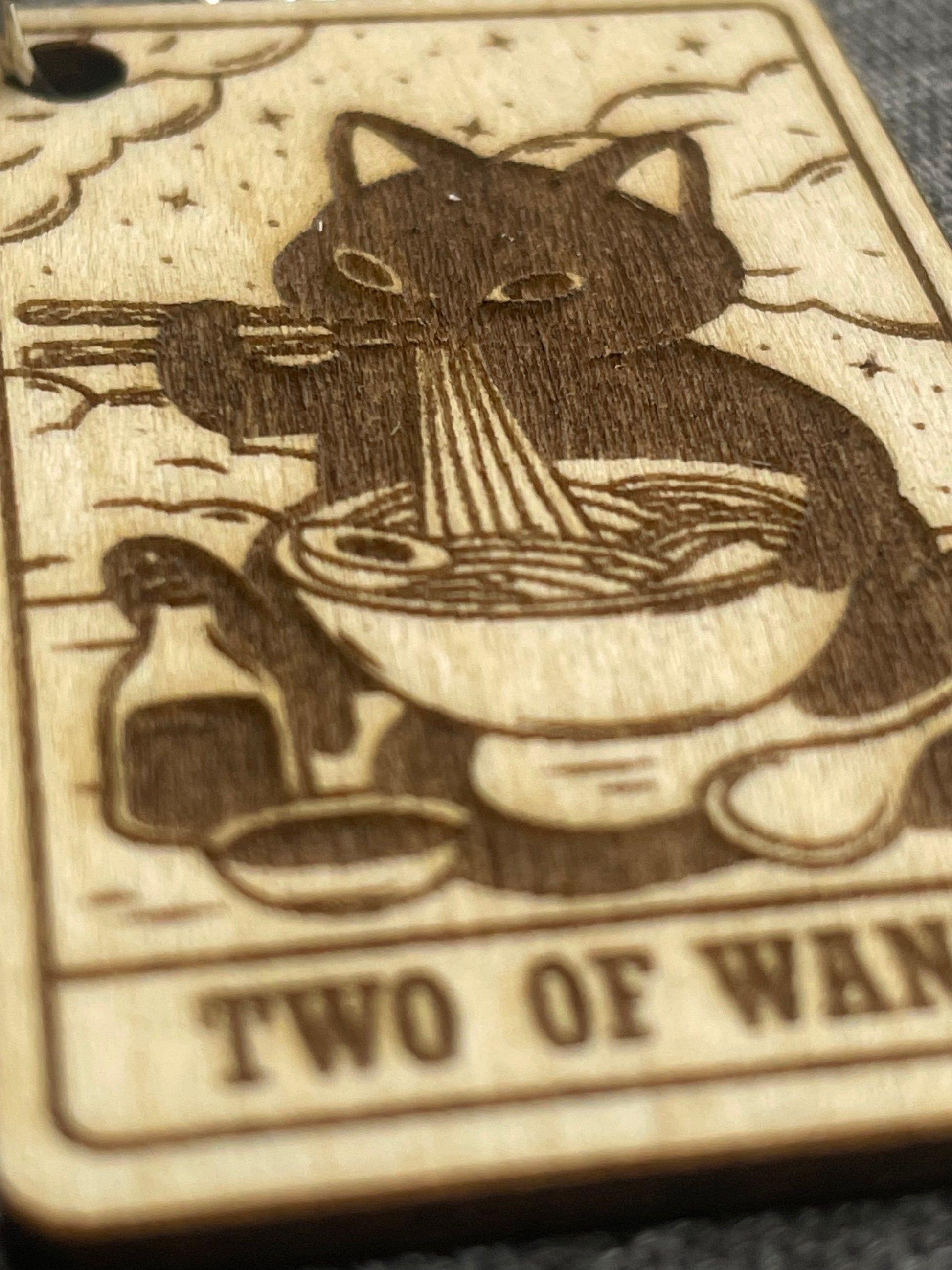 Wooden engraving of a cat and star pattern with text 'TWO OF WANDS' on a textured background.